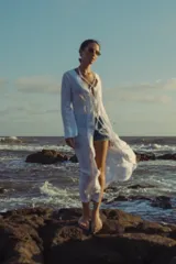 Vestido largo blanco con escote en V profundo y mangas largas acampanadas. Presenta aberturas en la parte delantera y detalles de cordones cruzados en el escote.