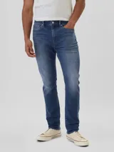 Jean de corte slim athletic en tono azul medio, con diseño de cinco bolsillos, cierre de cremallera y botón metálico.