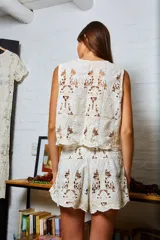 Chaleco de algodón color crema con calados y bordados florales, con lazos en el frente.