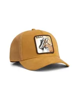 Gorra tipo trucker de color beige con frente de gamuza sintética y parte trasera de malla. Presenta un parche bordado en el frente con la imagen de una cabra y la inscripción G.O.A.T. sobre fondo dorado metálico.