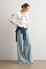 Remera blanca de manga corta con escote en V, decorada con delicados bordados florales en azul oscuro en el pecho, hombros y mangas.