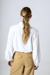 Camisa blanca de manga larga holgada, con cuello camisero, cierre frontal de botones y puños fruncidos con elástico.