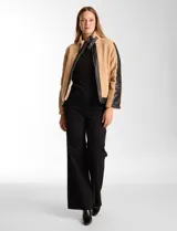 Campera de corderito sintético color beige con paneles y detalles en cuero sintético negro. Presenta cuello alto con tira y hebilla metálica, cierre frontal metálico y mangas largas con paneles de cuero sintético.