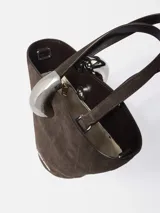 Bolso cubo asimétrico Jacquemus Le Petit de piel de ante marrón con relieve de cocodrilo. Tiene doble asa superior, asa bandolera extraíble, cierre de anilla metálica plateada y bolsillo interior con cremallera.