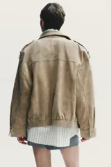 Cazadora de mujer confeccionada en piel de ante color gris oscuro con cuello subido, manga larga con trabillas en los hombros, bolsillos delanteros y con solapa en el pecho. Cierre frontal con cremallera y solapa con botones a presión.