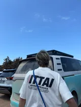 Remera marrón de corte holgado con estampado en la espalda que incluye la palabra "ITTAI" en blanco con líneas rojas y azules, la frase "AN IBIZA PRODUCE" y un texto más pequeño que dice "Ittai Stars Department Gallery - Ibiza Edition. If you're in Ibiza, 112 is not an option.".