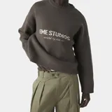 Sweater de punto grueso color marrón oscuro, con corte cuadrado y ligeramente corto. Presenta cuello redondo, puños y ruedo acanalados, y el logo de la marca Eme Studios junto a la frase 'curated by ben ice' en jacquard color crema en el frente.