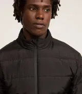 Campera acolchada tipo puffer, color marrón topo, con cuello alto y cierre frontal de cremallera. Presenta costuras horizontales que crean un efecto acolchado.