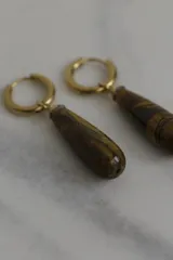 Aros tipo argolla con dije colgante en forma de gota de piedra natural ojo de tigre, con estructura de acero quirúrgico en tono dorado.