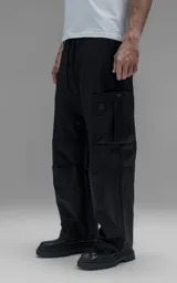 Pantalón cargo de corte regular confeccionado en textil técnico pesado. Presenta cintura elástica con cordón de ajuste, bolsillos laterales en la cintura y bolsillos cargo de gran tamaño en los muslos. Incluye elásticos con tancas en los tobillos para regular la apertura de la pierna.