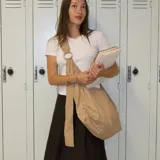 Bolso de hombro tipo hobo color beige, confeccionado en nylon arrugado, con bolsillo externo frontal y correa ajustable con argolla decorativa.