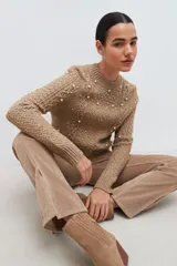Sweater color beige melange de tejido de punto con diseño de trenzas y detalles de perlas en el frente y las mangas.