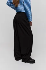 Pantalón sastrero de pierna amplia, color negro, con tiro medio, cintura con pasacintos, cierre frontal con botón y cremallera, bolsillos laterales y bolsillos ojal decorativos en la parte posterior.