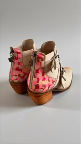 Botas de cuero natural color blanco marfil con diseño artístico pintado a mano en la parte trasera en tonos rosados y marrones, taco de madera y hebillas metálicas laterales.