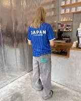 Camiseta de fútbol de manga corta en color azul con diseño estampado abstracto y cuello en V rosado con detalles blancos a juego con los puños. Presenta inscripciones y escudos deportivos en el pecho.