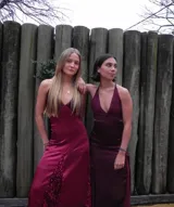 Vestido largo sin mangas con escote en V halter y aberturas laterales (cut-outs) en la cintura. El cuerpo superior presenta un llamativo diseño estampado multicolor, mientras que la falda larga es de tejido texturizado brillante en color verde esmeralda con inserciones godet en el ruedo.