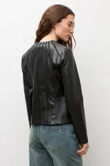Chaqueta negra de cuero sintético, de manga larga, con detalle de pliegues en la parte frontal y cierre con cremallera.