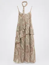 Conjunto compuesto por un vestido largo sin mangas de estampado paisley con volados en capas y un pañuelito a tono, acompañado por una chaqueta beige de manga corta con solapas, botón frontal y bolsillos.