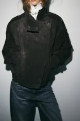Cazadora tipo biker confeccionada en piel de ante 100%, con cuello subido, cierre frontal cruzado con cremallera y botones forrados. Presenta mangas largas con trabillas en los hombros, bolsillos de vivo en el delantero y bajo acabado en elástico.
