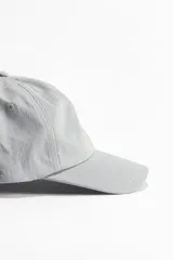 Gorra gris de sarga de algodón con ojales bordados y trabilla ajustable con cierre de metal en la parte trasera.