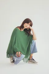 Poncho tejido de punto en color verde, con diseño holgado, cuello redondo y terminación con flecos en el ruedo.