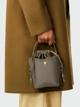 Minibolso tipo bucket de piel lacada color gris, con cierre de cordón ajustable y detalle de logo metálico dorado en forma de corazón con letra A. Cuenta con asa superior fija.