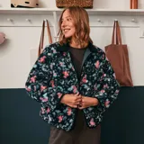 Chaqueta corta con estampado floral en tonos rosa y celeste sobre fondo negro. Tiene cuello mao y cierre frontal con botones a presión.