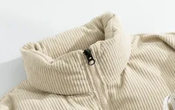 Campera puffer marrón con paneles horizontales acolchados. La parte superior de la espalda es de pana marrón con el texto 'Chingona' bordado en blanco. Posee cordón ajustable en el ruedo y se lleva superpuesta a una sudadera con capucha gris.