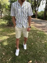 Camisa de manga corta con diseño a rayas verticales en tonos verde militar y blanco, cuello camisero con solapa abierta y cierre frontal con botones.