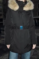 Anorak acolchado negro resistente al agua y al viento, con cuello subido y capucha con pelo sintético en tono tostado a contraste. Cuenta con manga larga, bolsillos delanteros con cierre, cinturón elástico ajustable con hebilla metálica y cierre frontal con cremallera y botones a presión ocultos.