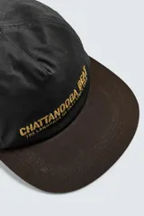 Gorra de algodón negra con visera plana de color marrón oscuro. Presenta bordado frontal en hilo dorado con el texto "CHATTANOOGA BEAT THE LANGUAGE OF JAZZ SINCE 1920".