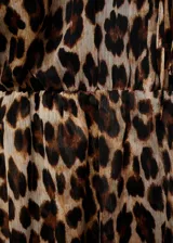 Vestido corto de tejido fluido con estampado animal print de leopardo. Presenta cuello redondo con cierre de lazo, mangas largas con puños elásticos y volados, y diseño evasé con falda de capas.