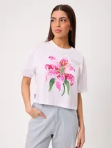 Remera blanca de algodón con estampado frontal de una flor rosa y verde, de corte holgado y mangas cortas.