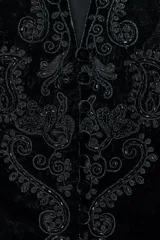 Chaleco de terciopelo negro con escote en pico y manga sisa. Presenta bordados ornamentales a tono en el frente y los bordes. Cuenta con cierre frontal de botones y forro interior.