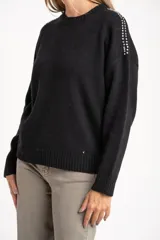 Sweater de lana color negro, de corte oversize, con cuello redondo, mangas largas y detalle de apliques metálicos en los hombros.