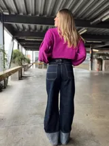 Pantalón de jean ancho, tiro alto, color azul oscuro, con pespuntes contrastantes en color claro. El ruedo está doblado mostrando el revés de la tela en tono gris claro.