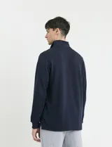Remera de manga larga con cuello polo, confeccionada en tejido de punto canalé francés. Presenta abotonadura frontal con botones de madera y detalles a contratono en la cartera y el interior del cuello.