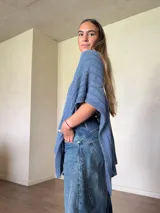 Ruana tejida de algodón con hilo lurex en punto jersey, color azul, con diseño amplio y detalle de etiqueta de cuerina en la parte posterior.