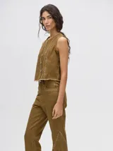 Pantalón de denim color marrón, de tiro alto y calce ochentoso con terminación estilo oxford. Cuenta con apliques metálicos decorativos alrededor de los bolsillos y a lo largo de las costuras exteriores.