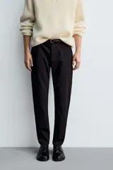 Pantalón de corte slim fit y color negro, confeccionado en tejido elástico. Cuenta con cintura elástica, trabillas, bolsillos frontales y cierre con cremallera y botón.