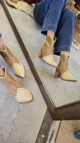 Bota tejana de cuero combinado en napa y croco, con puntera y caña en tonos beige y tostado, y detalle metalizado dorado. Presenta tachas decorativas en la puntera y el empeine, y cuenta con taco de madera de 6,5 cm.