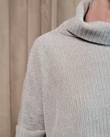 Polera de tejido suave con textura acanalada, cuello alto tipo tortuga, mangas largas y corte holgado con aberturas laterales en el ruedo.