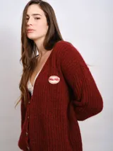 Cardigan de punto color bordó con escote en V, cierre frontal con botones y parche decorativo con texto en el pecho. Presenta mangas largas y diseño holgado.