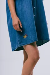 Vestido corto de denim azul oscuro, con cuello camisero, mangas cortas, cierre frontal con botones, bolsillo aplicado en el pecho y calce holgado.