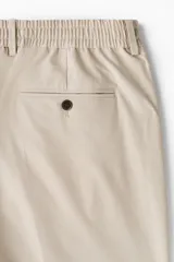 Pantalón de vestir color beige, de corte relajado, con bolsillos laterales y traseros, y raya marcada en las piernas.