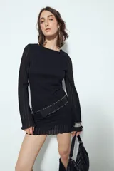 Vestido corto de punto color negro, con silueta ajustada y mangas largas acampanadas. Presenta una textura de tejido liviano con diseño de líneas verticales y cuello redondo.