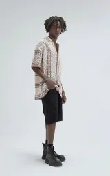 Camisa de manga corta tejida en punto abierto (símil crochet), color beige con detalles en marrón. Presenta cuello solapa, cierre frontal con botones y calce oversize.