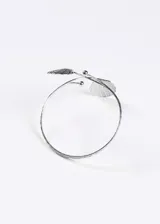 Brazalete abierto de metal plateado con diseño de dos almejas en los extremos y estructura de doble línea texturizada.