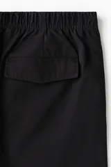Pantalón en mezcla de algodón color negro, con cintura elástica con cordón de ajuste y botón. Presenta bolsillos laterales discretos y costuras giradas en las piernas, con un corte relajado.