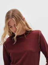 Polera de manga larga confeccionada en tela rib color bordó, con cuello alto y hombreras. Presenta costuras a la vista con pespuntes en hilo de color contrastante en el cuello, puños, hombros y ruedo.